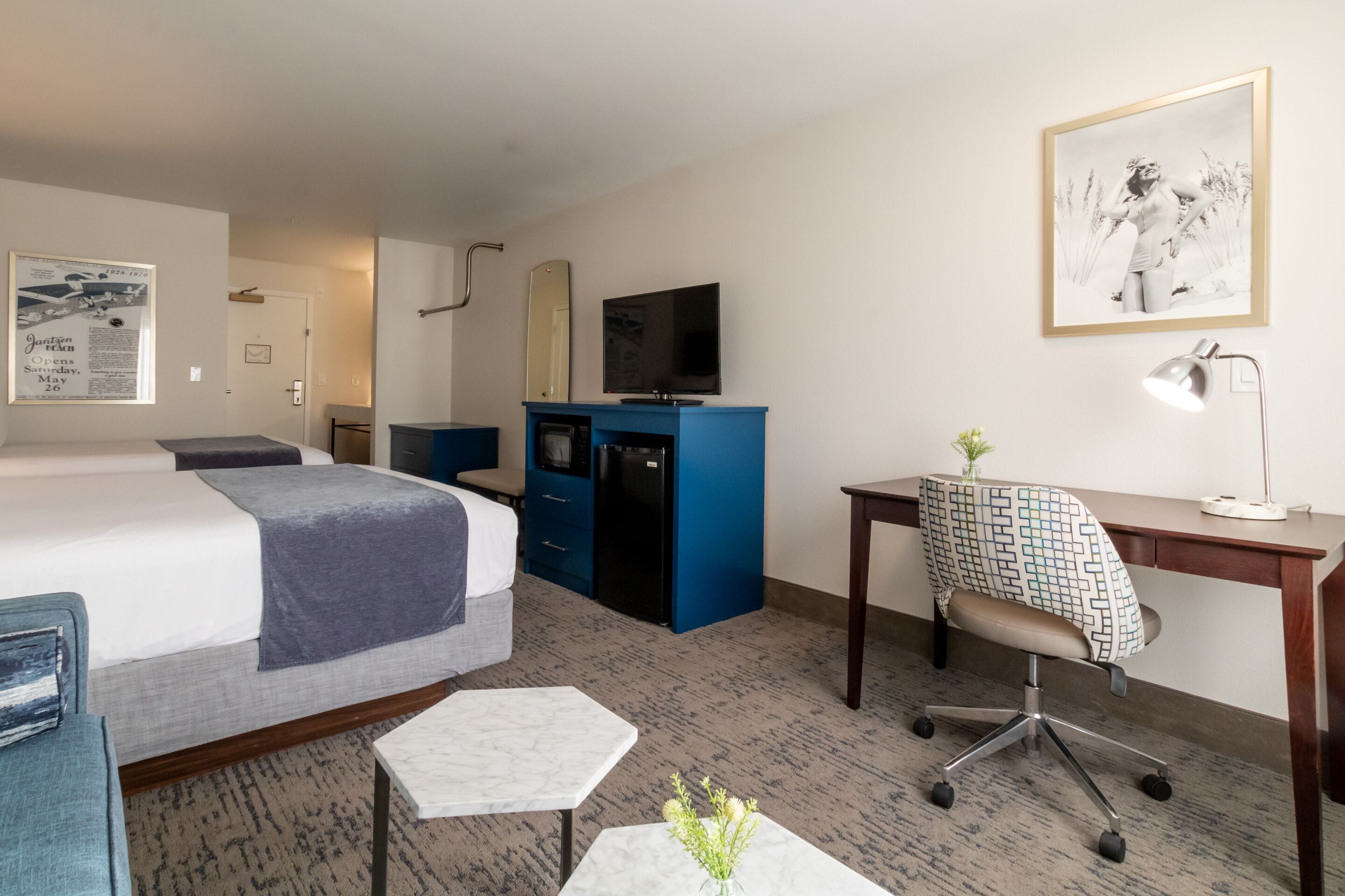 Une chambre d’hôtel avec un lit, un bureau, une chaise, une télévision, un miroir et un tableau encadré au mur.