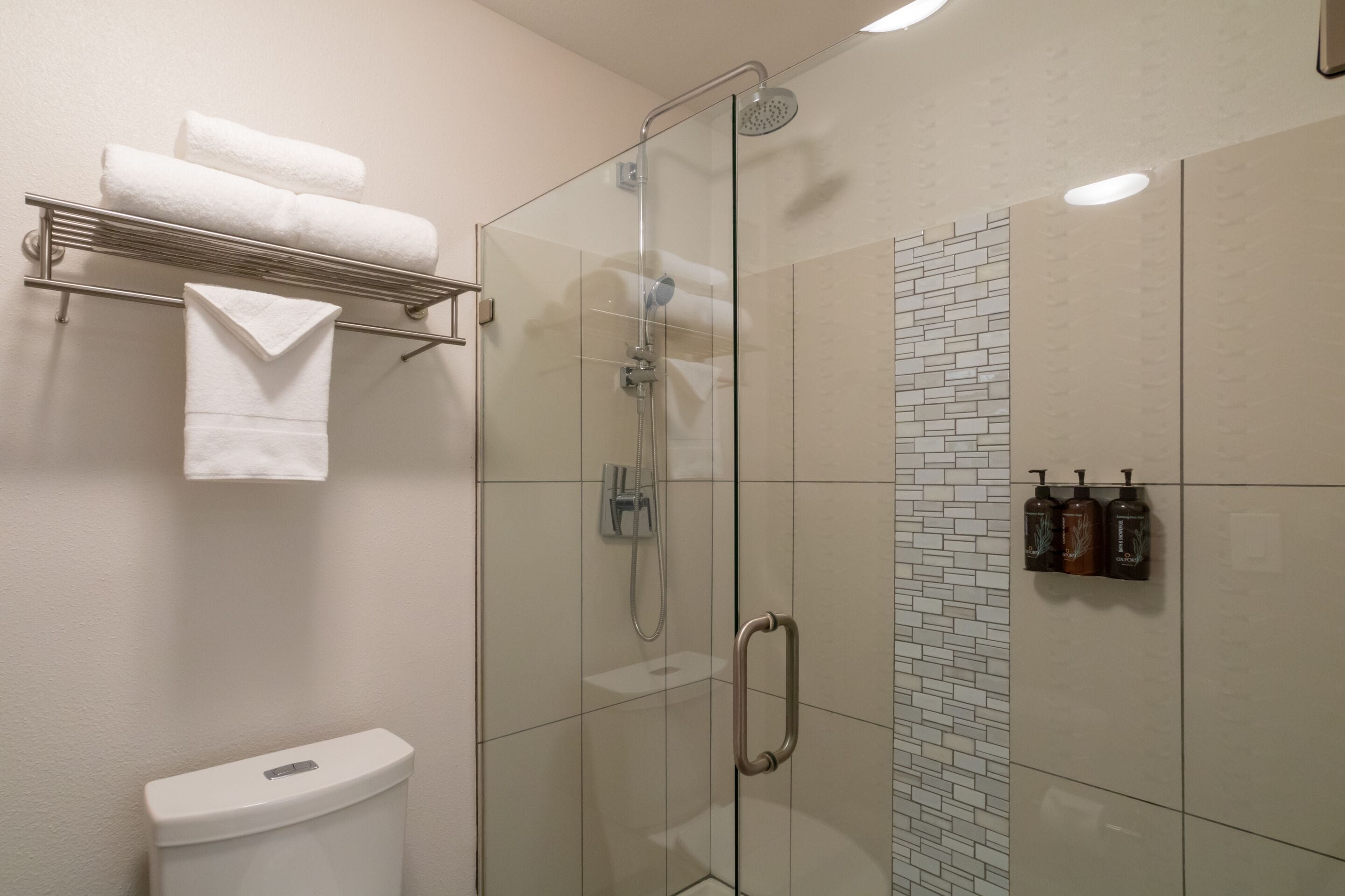 Une salle de bain moderne avec une douche à parois de verre, des toilettes et un porte-serviettes avec des serviettes pliées.