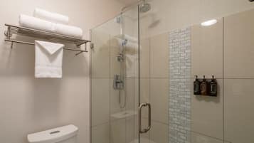 Un baño moderno con ducha acristalada, inodoro y toallero con toallas dobladas.