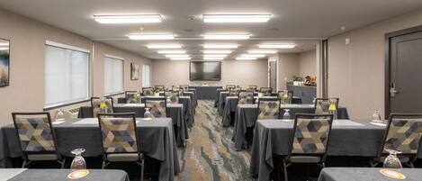 Un salón de conferencias con varias mesas y sillas, con iluminación en el techo y una pantalla grande al frente.