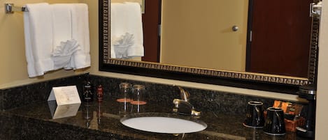 A bathroom with a granite countertop, a sink, a mirror, and two white towels hanging on a rack.