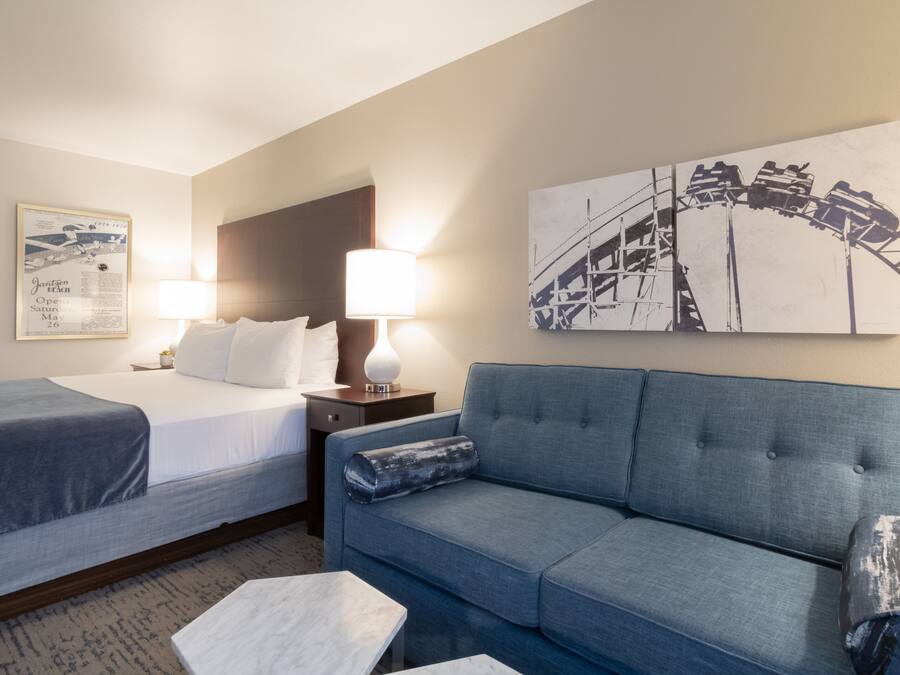 A hotel room with a bed, two bedside tables with lamps, a sofa, and a large wall art piece.