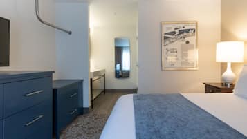 Habitación de hotel con cama, tocador, espejo, mesita de noche con lámpara y un cartel en la pared.