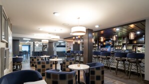 A modern restaurant interior with round tables, blue upholstered chairs, and pendant lighting. - Oxford Suites Portland - Jantzen Beach (Portland)