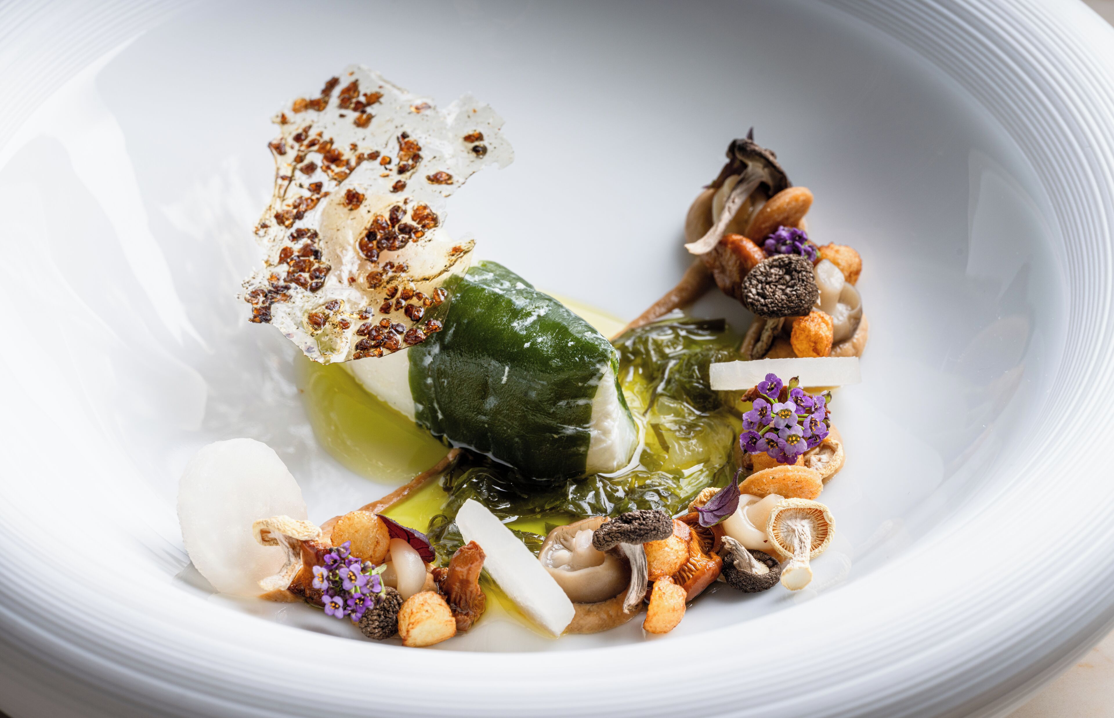 A white plate with a variety of food items including a green vegetable, nuts, and some purple flowers.