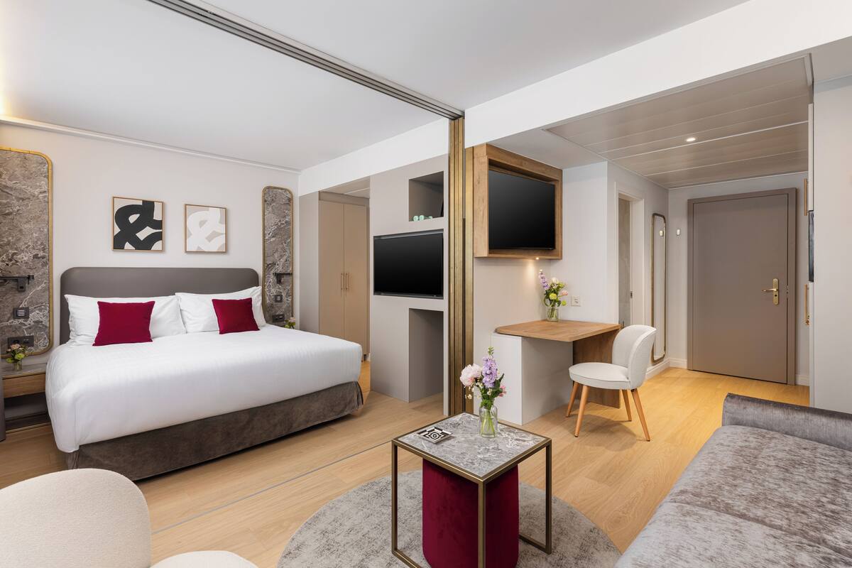 Moderni hotellihuone, jossa on sänky, työpöytä, televisio ja sohva.
