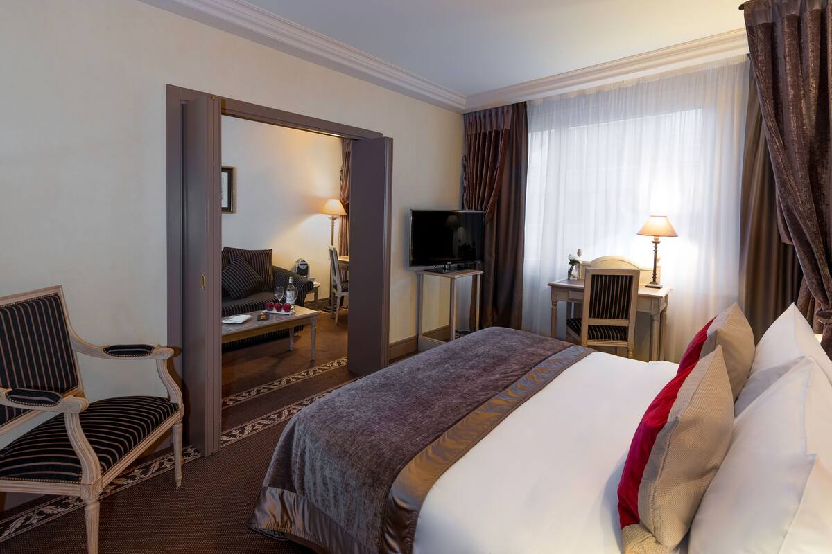 Hotellihuone, jossa on sänky, tuoli, lamppuvarusteinen työpöytä, televisio ja peili.
