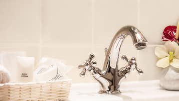 Une salle de bain dotée d’un robinet chromé moderne, d’un lavabo blanc et d’un panier contenant des articles de toilette, notamment un flacon de lotion pour le corps.
