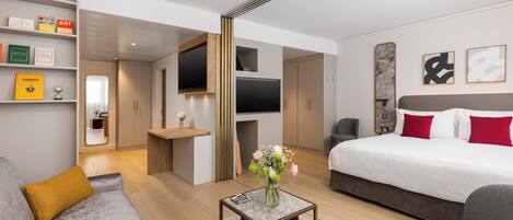Una habitación de hotel moderna con una cama grande, un sofá, un televisor y una pequeña mesa con un jarrón de flores.