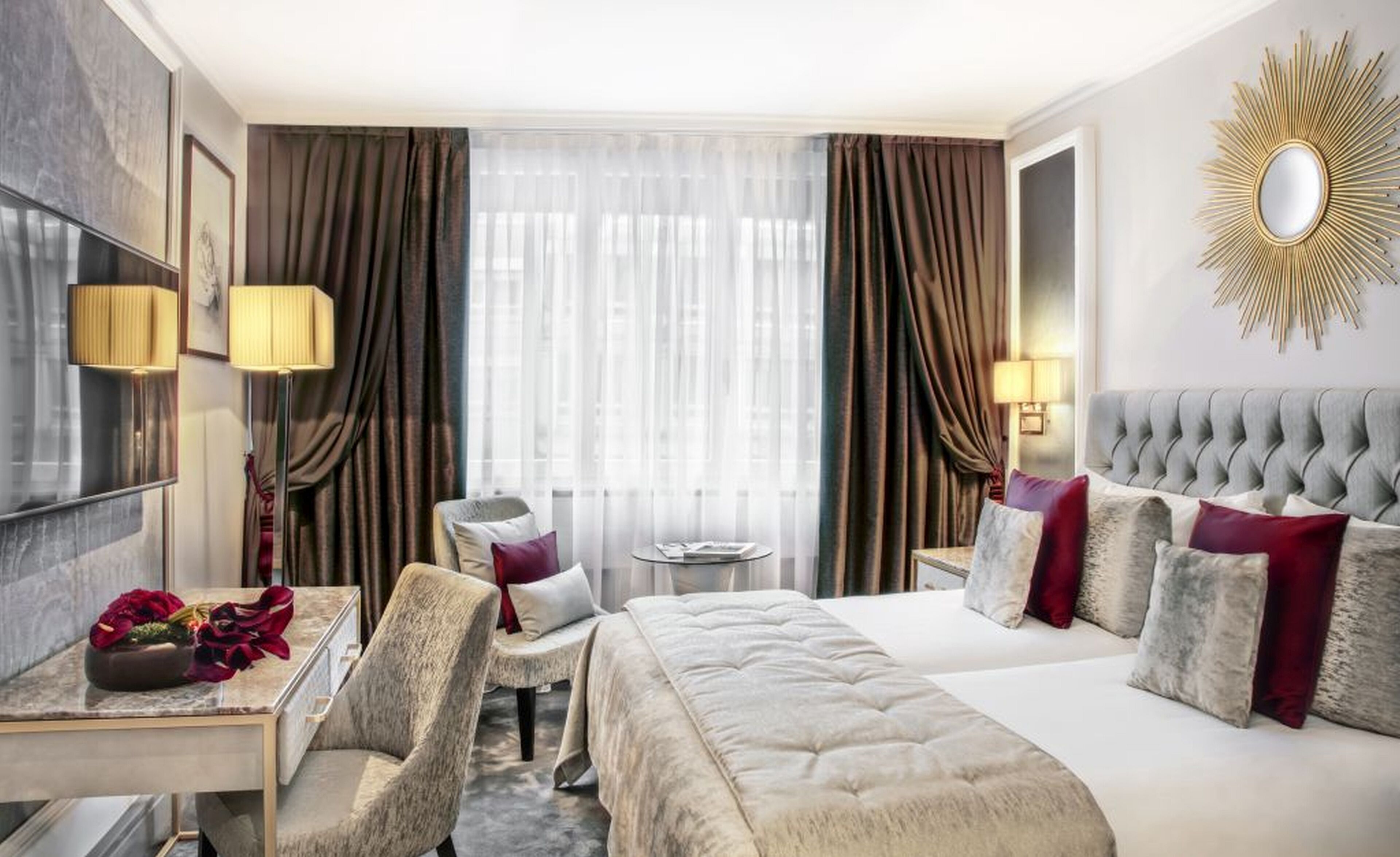 A hotel room with a large bed, a desk with a chair, a small table, and a TV.