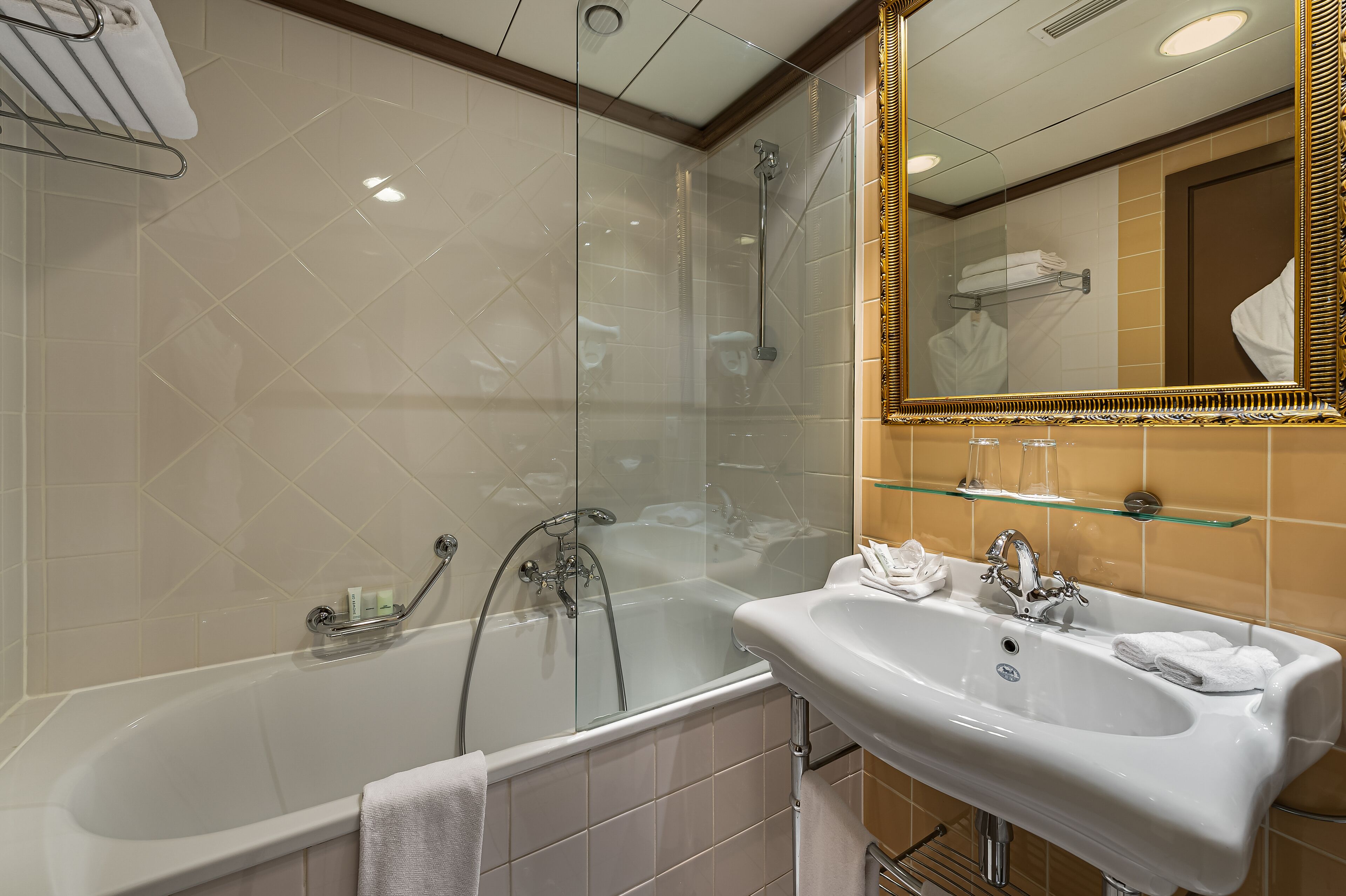 Une salle de bain moderne avec une douche en verre, un lavabo blanc et un miroir avec un cadre doré.