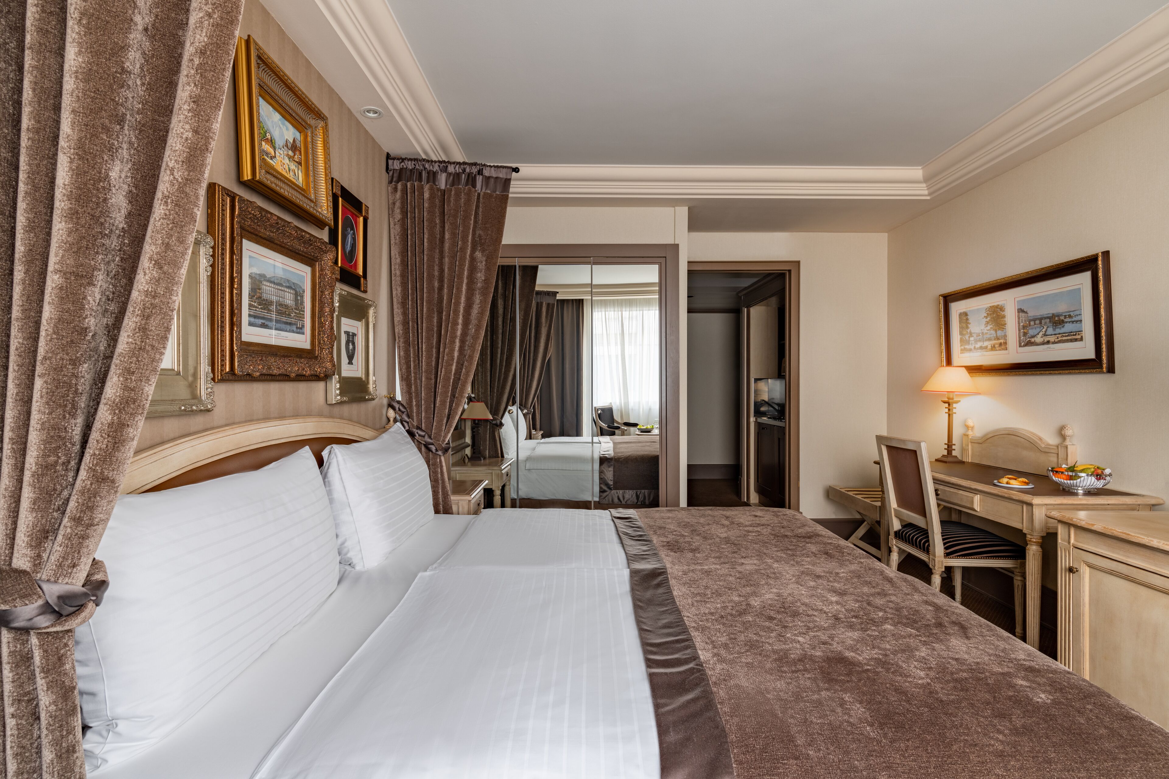 A hotel room with a large bed, a desk with a chair, a mirror, and framed pictures on the wall.