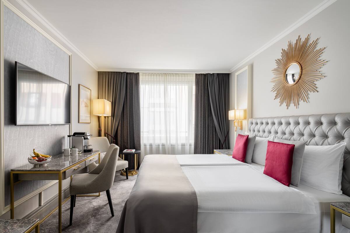 Hotellihuone, jossa on suuri sänky, työpöytä tuolilla, televisio ja seinällä koristeellinen peili.