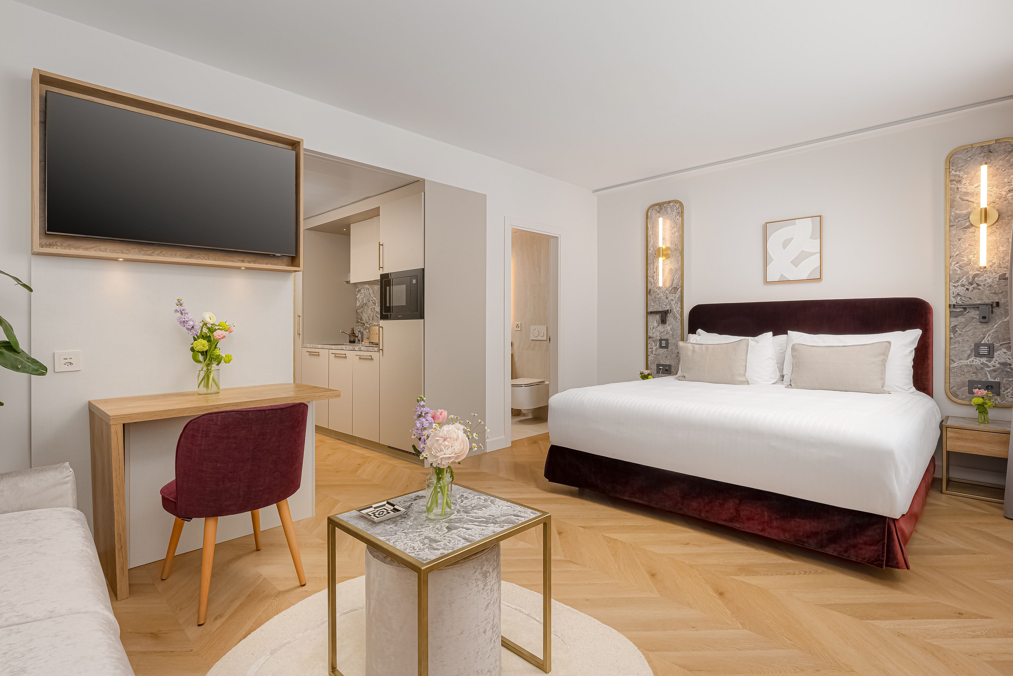 Une chambre d’hôtel avec un lit, un bureau, une chaise, une télévision et une petite table agrémentée de fleurs.