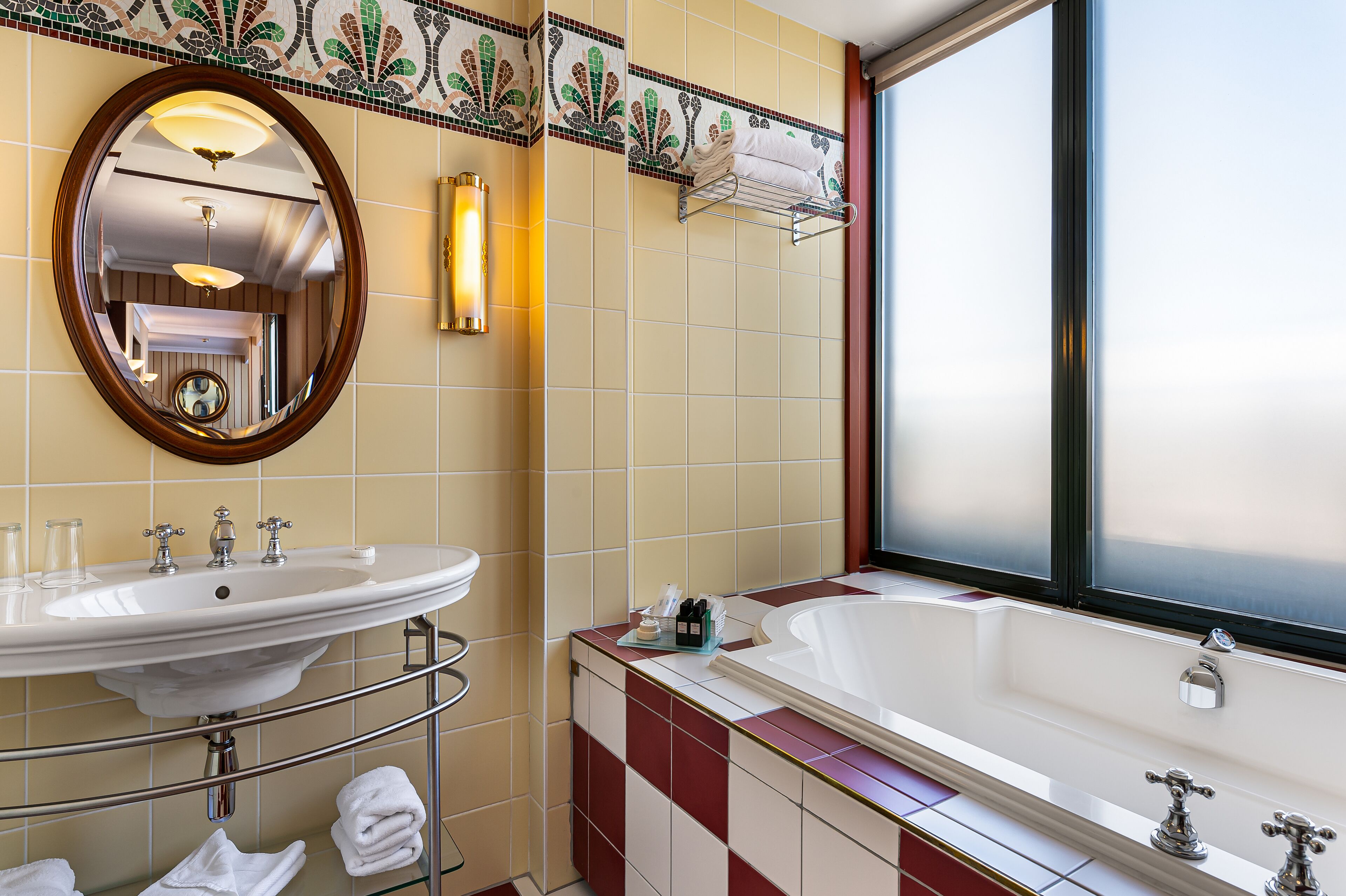 A bathroom with a large oval mirror, a sink, a bathtub, and a window.