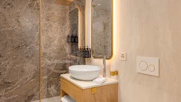 Une salle de bain avec un mur en marbre, un lavabo blanc et un miroir encadré d’or.