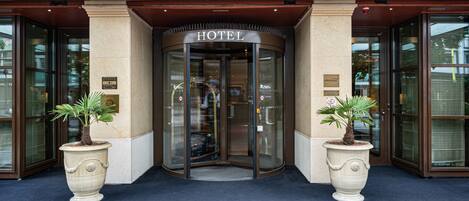 A hotel entrance with a revolving door, large potted plants, and a sign indicating the hotel's name.