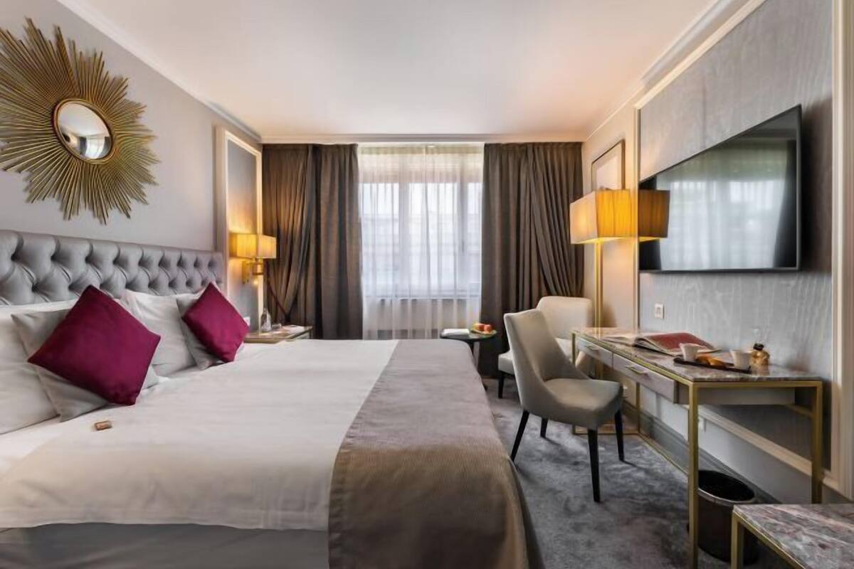 Hotellihuone, jossa on suuri sänky, työpöytä, tuoli, televisio ja aurinkomallinen peili.