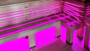 Una sauna de madera con un banco con forma de flamenco rosa e iluminación ambiental rosada.