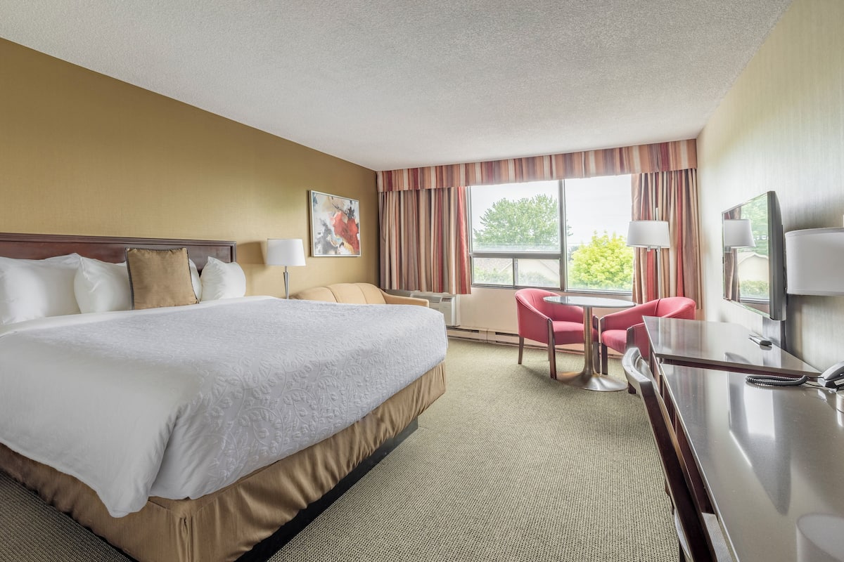 Une chambre d’hôtel avec un grand lit, un bureau avec un téléphone, une chaise et une fenêtre avec des rideaux.