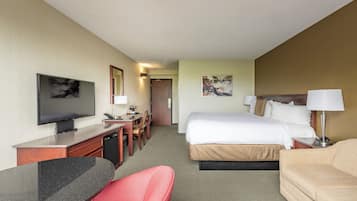 A hotel room with a bed, a desk with a television, a chair, a sofa, and a painting on the wall.