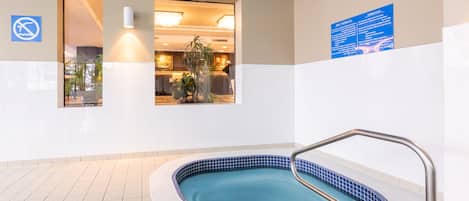 Une piscine avec un escalier en métal, un panneau indiquant qu’il est interdit de se baigner, et un espace d’accueil visible à travers une porte.