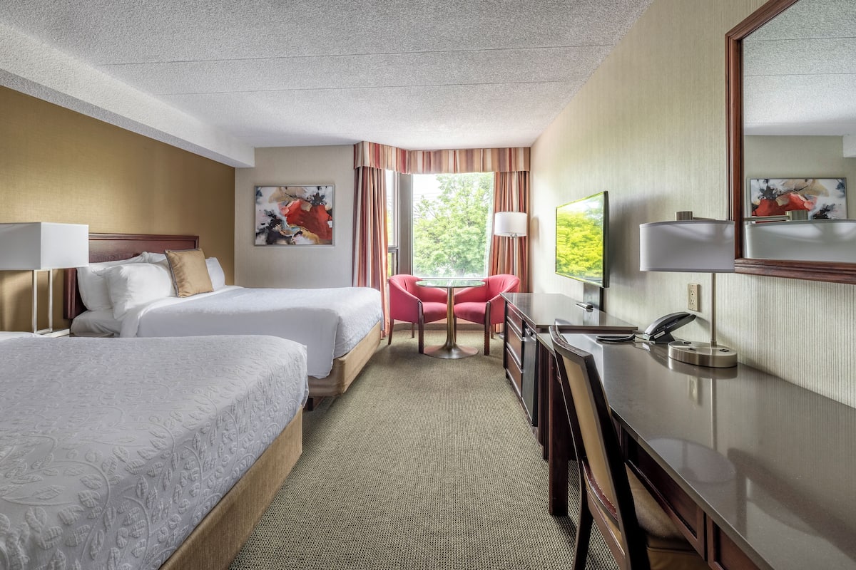 Une chambre d’hôtel avec deux lits, un bureau, une chaise, un miroir et une fenêtre avec des rideaux.