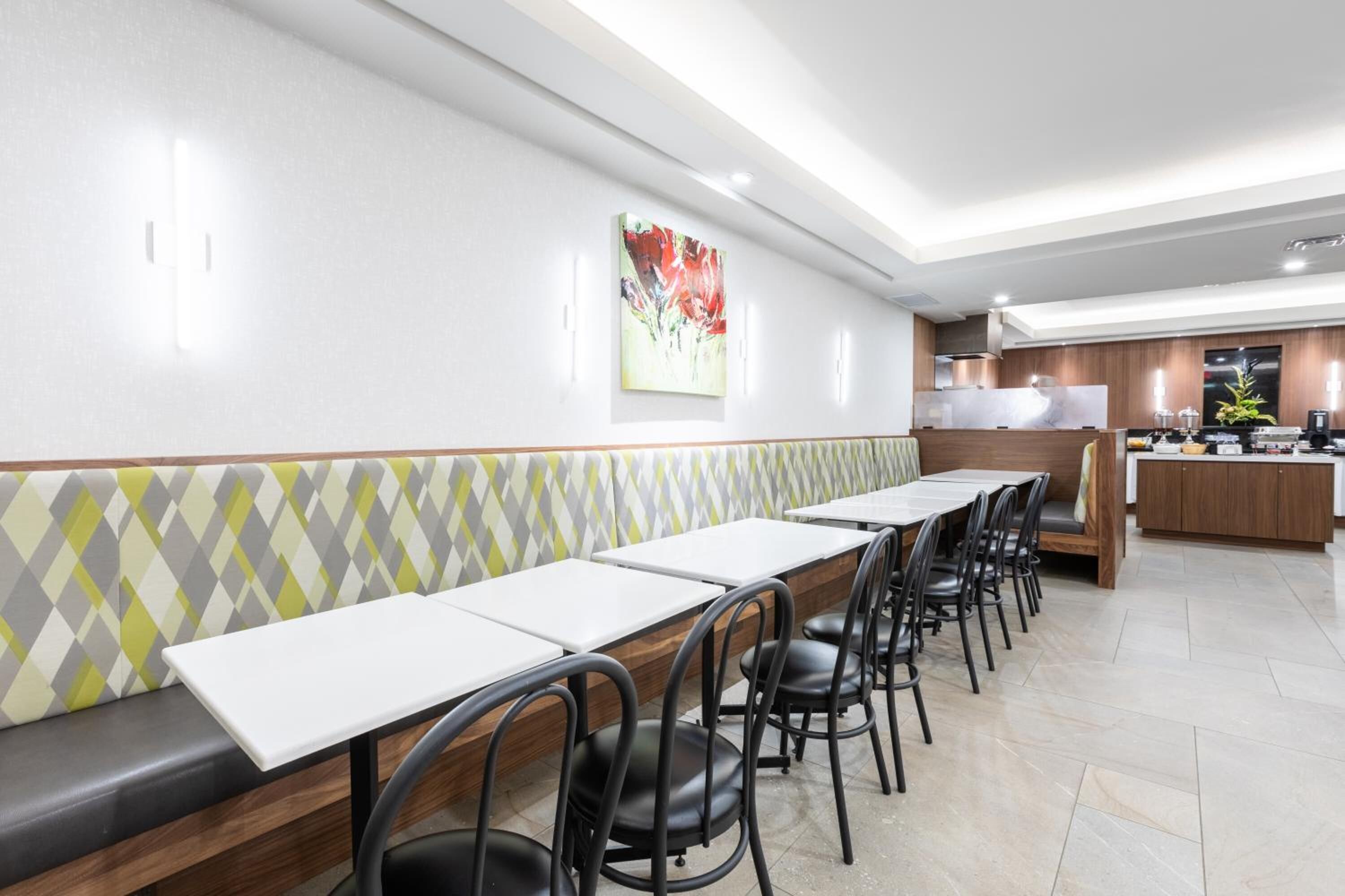 Un restaurante moderno con una barra larga, sillas negras y una zona de cocina al fondo.