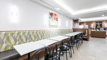 Un ristorante moderno con un lungo bancone, sedie nere e una zona cucina sullo sfondo.
