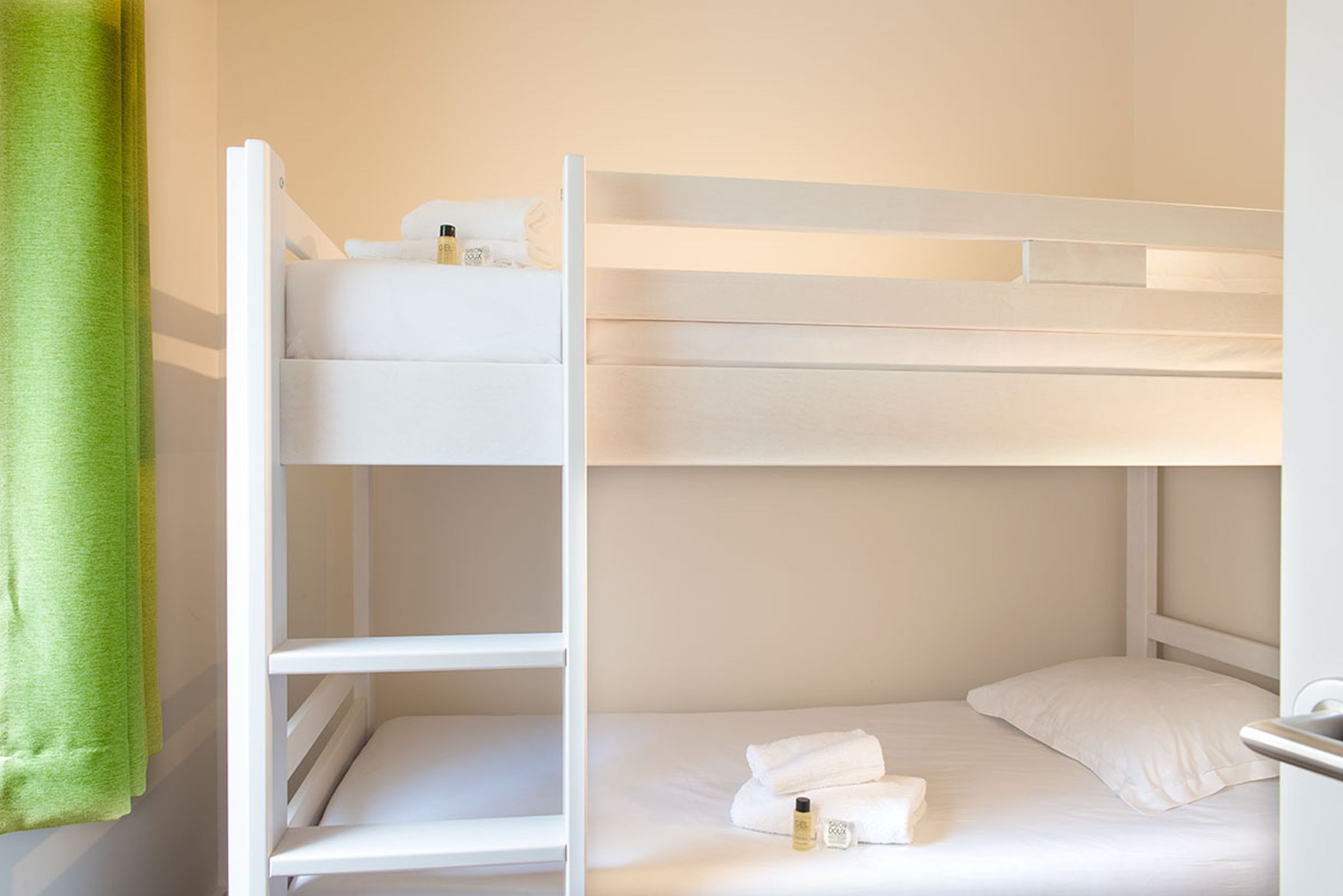 A bunk bed room with white bedding and a green towel.