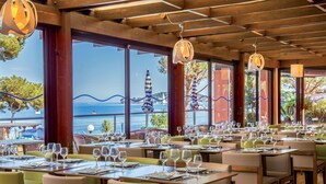 A restaurant with tables set for dining, large windows offering a view of the sea, and hanging pendant lights. - Hôtel Vacances Bleues Delcloy (Saint-Jean-Cap-Ferrat)
