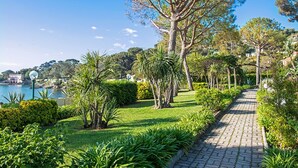A paved pathway lined with greenery and trees, leading towards a body of water. - Hôtel Vacances Bleues Delcloy (Saint-Jean-Cap-Ferrat)