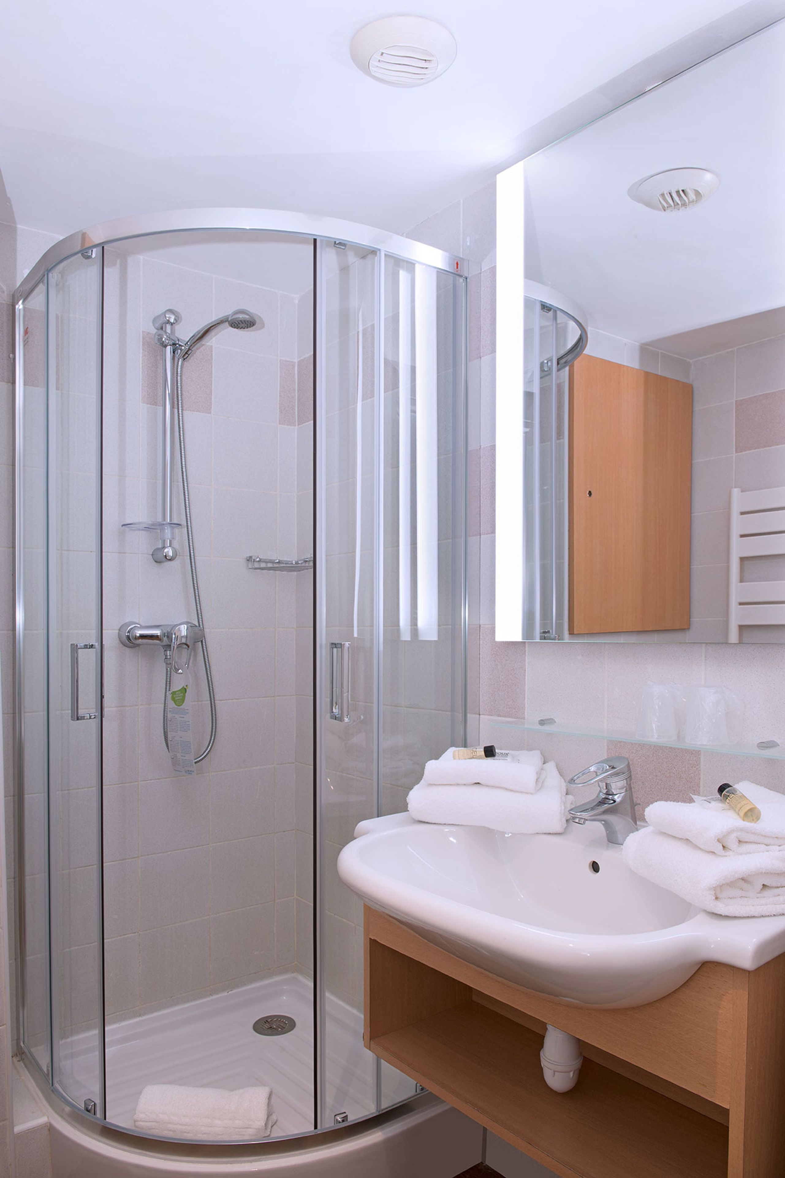 A modern bathroom with a glass-enclosed shower, a white sink, and a wooden vanity.