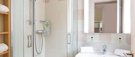 Un baño moderno con ducha de vidrio, lavamanos blanco y un espejo grande.