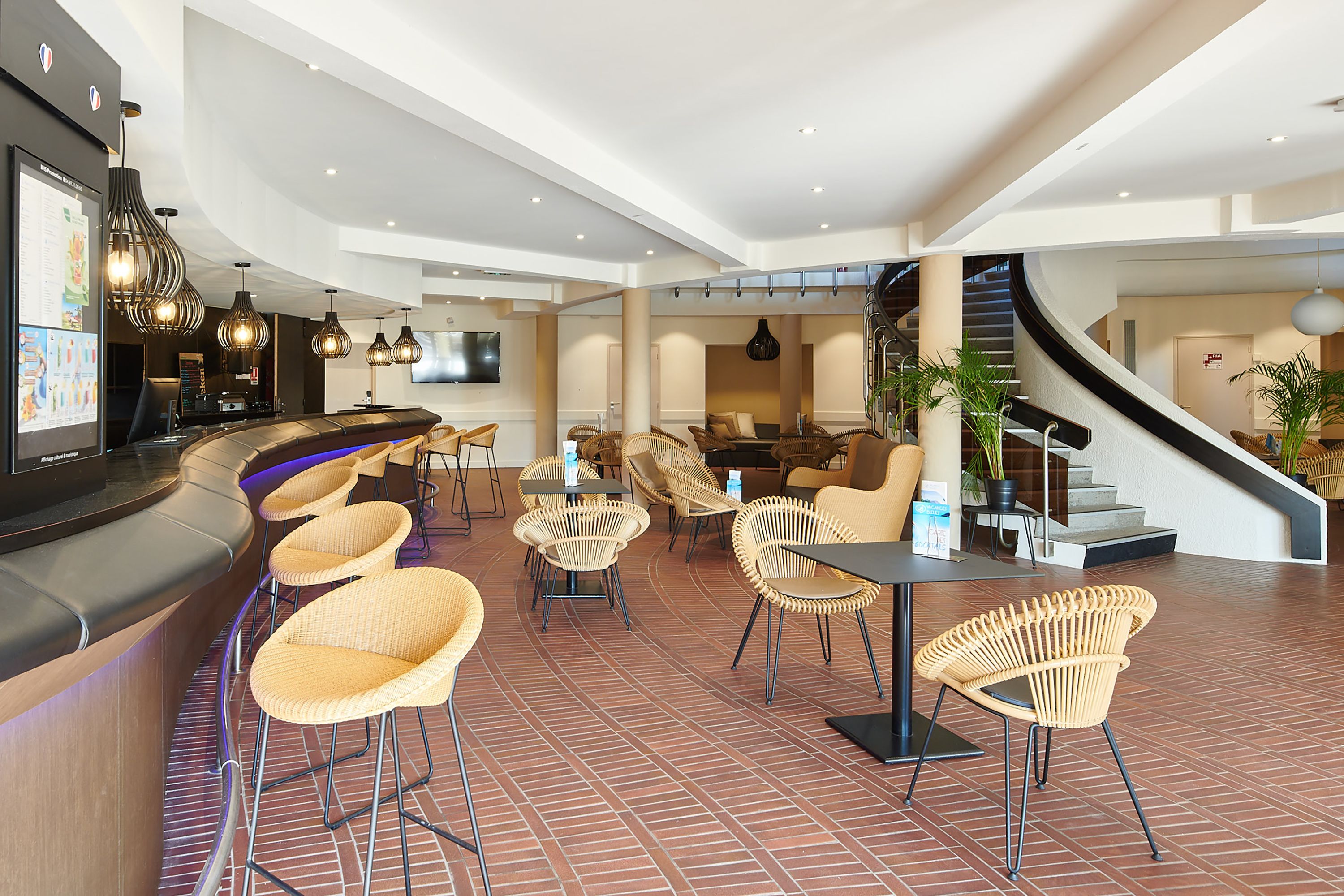 Un hall d'hôtel moderne avec un bar aux lignes courbes, des fauteuils en osier et un escalier.