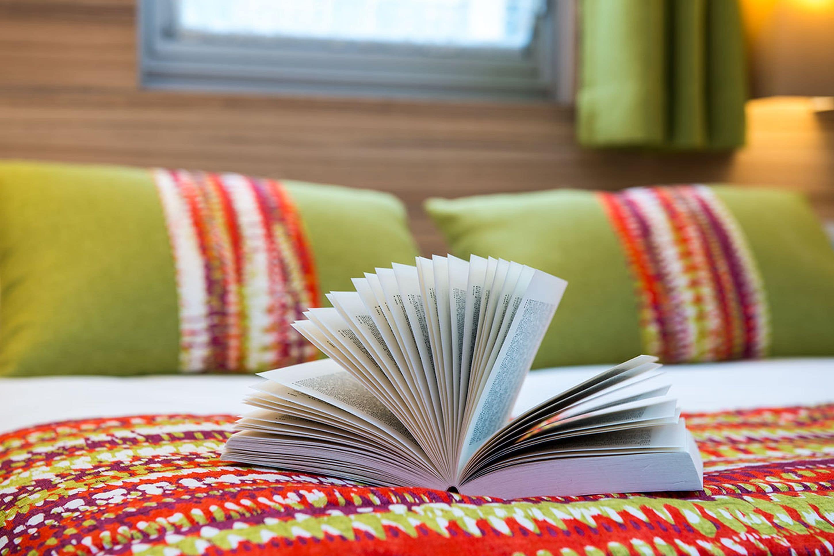 An open book on a bed with a colorful patterned bedspread.