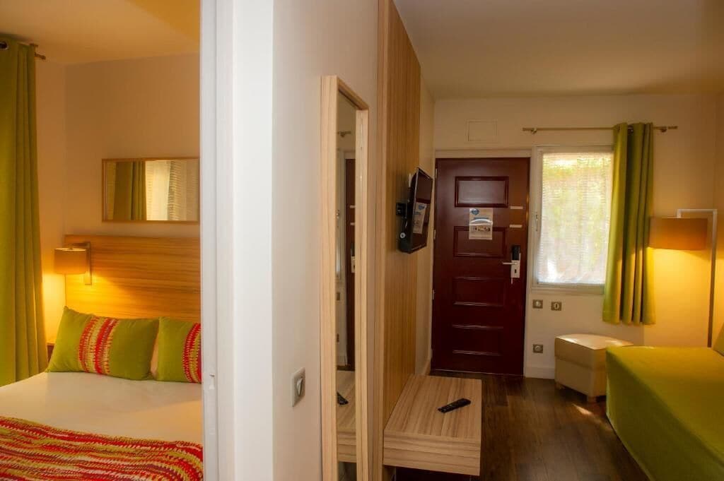 A hotel room with a bed, a desk, a TV, and a door leading to another room.