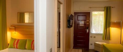 A hotel room with a bed, a desk, a TV, and a door leading to another room.