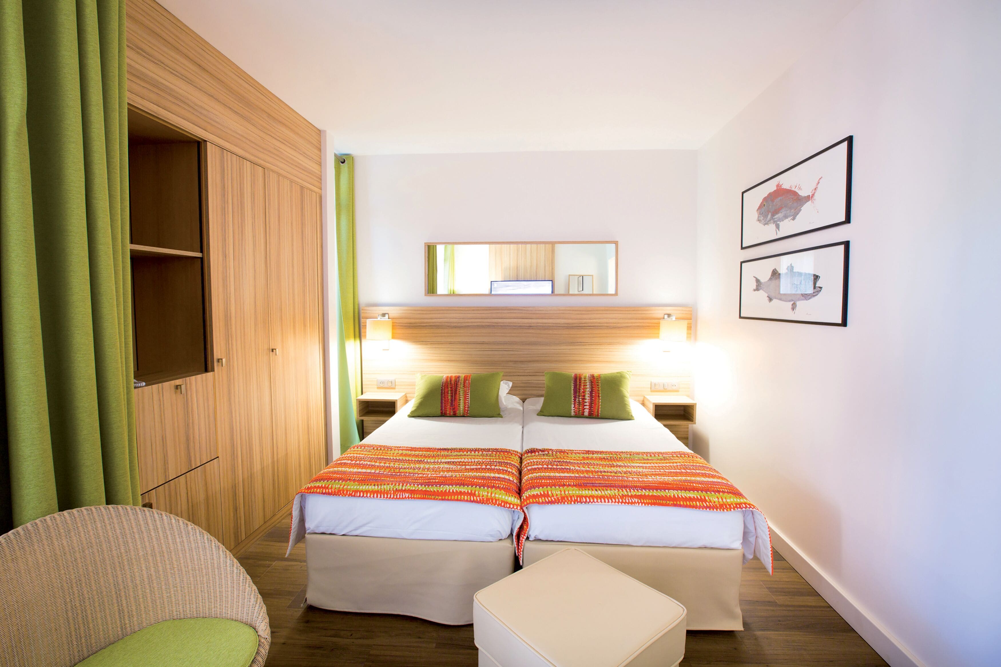 Ein Hotelzimmer mit Holzschrank, Bett mit zwei Kissen, Nachttisch, Sessel und einem kleinen Tisch.