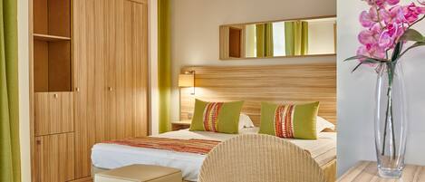 A hotel room with a bed, a green chair, a small table, and a wardrobe.