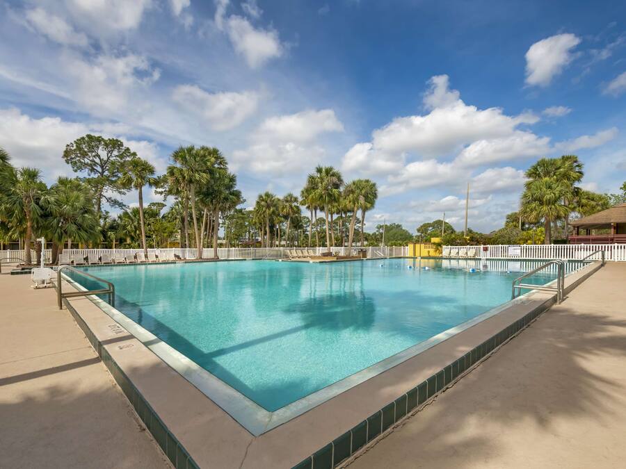 A rectangular swimming pool with clear blue water, surrounded by a white fence and palm trees.