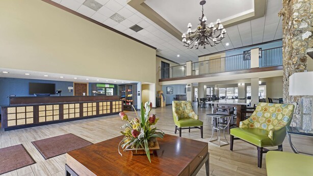 A hotel lobby with a reception desk, seating area, and a staircase to an upper level.