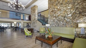 A spacious lobby with a high ceiling, stone walls, a staircase, and a variety of seating options including a sofa and chairs.