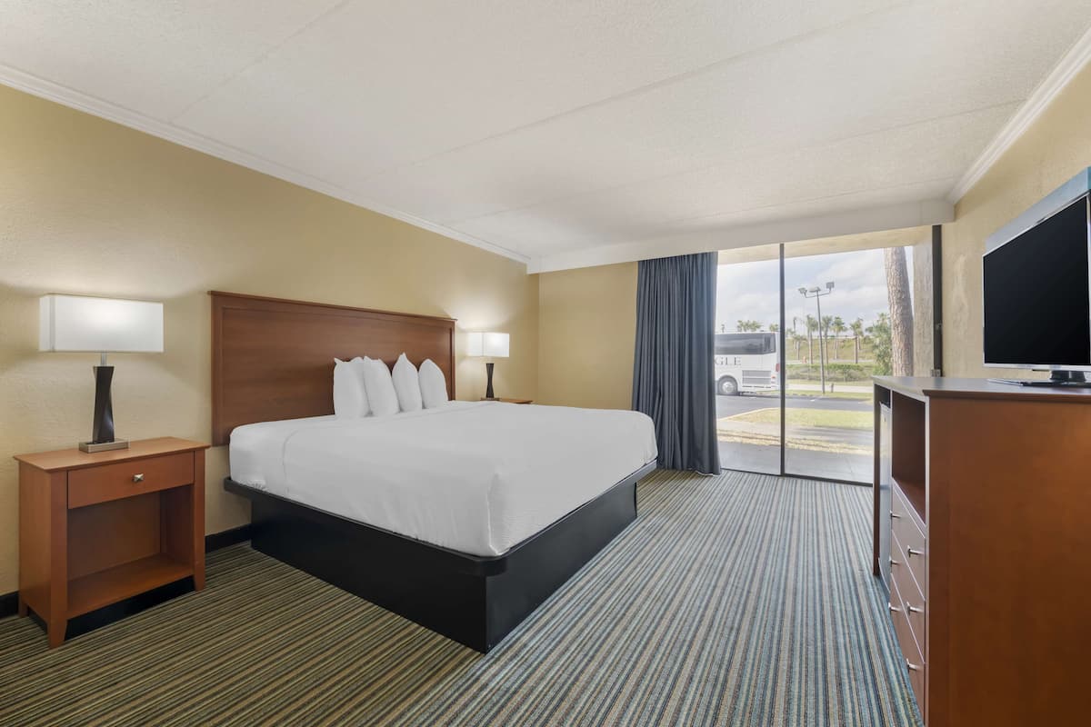 A hotel room with a large bed, two bedside tables with lamps, a TV, and a view of the parking area.