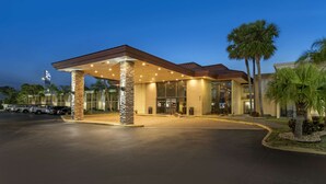 A hotel entrance with a covered fuel station, palm trees, and a clear sky.