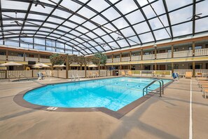 An indoor swimming pool with a glass ceiling, multiple balconies, and lounge areas.