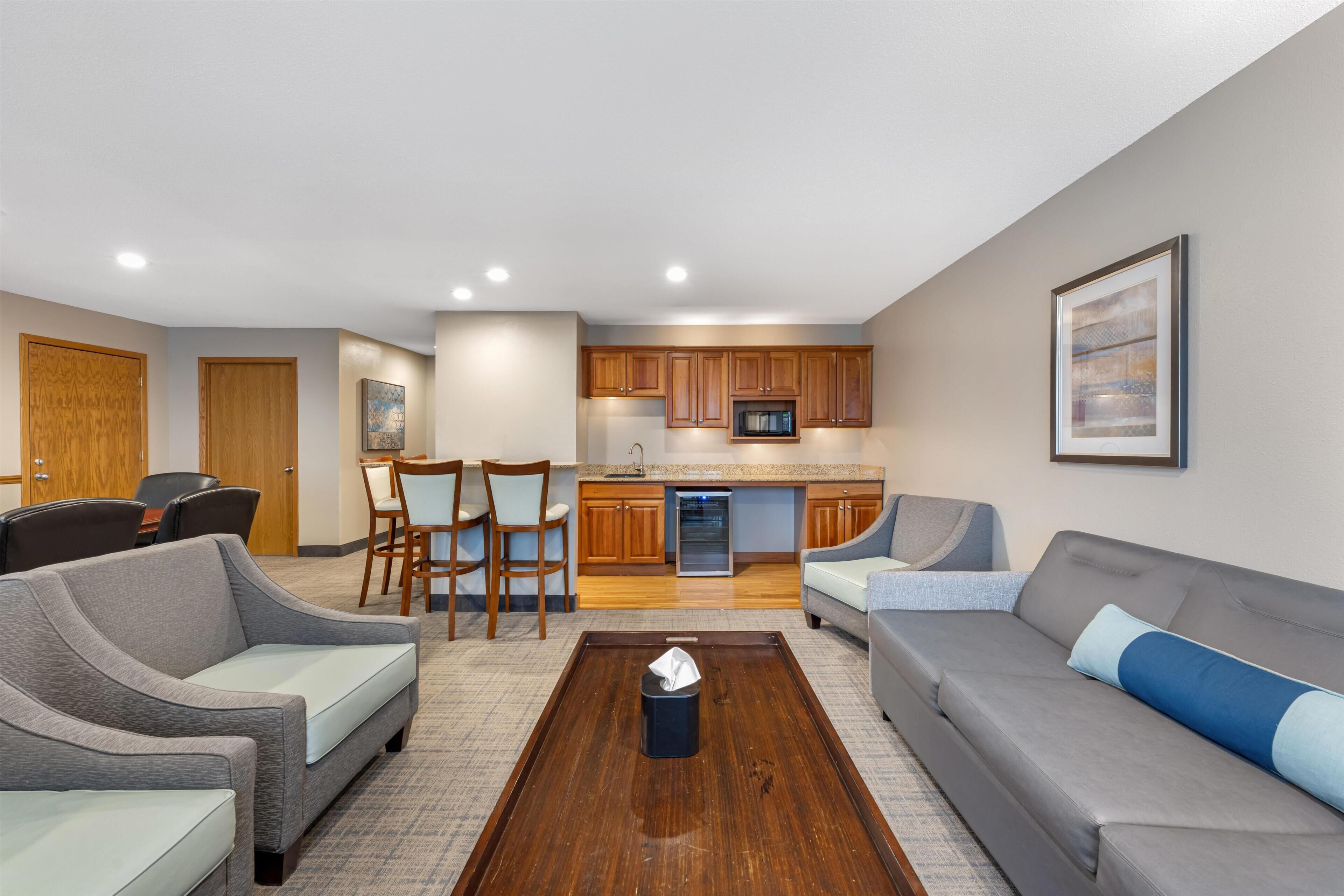 A modern living room with a grey sofa, a coffee table, and a dining area with wooden cabinets and chairs.