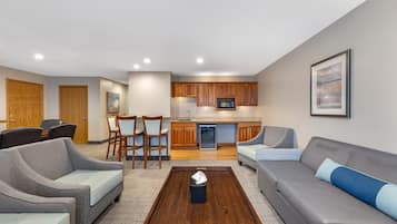 A modern living room with a grey sofa, a coffee table, and a dining area with wooden cabinets and chairs.