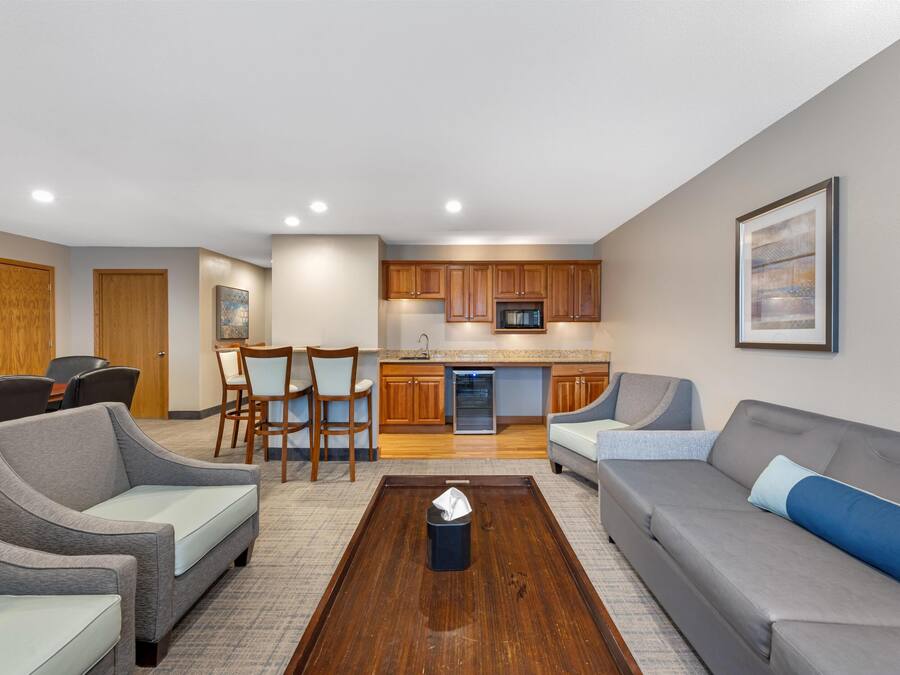 A modern living room with a grey sofa, a coffee table, and a dining area with wooden cabinets and chairs.
