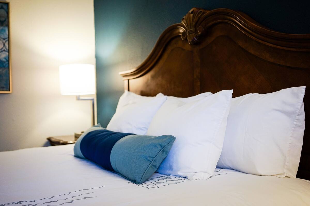 A bed with white and blue pillows, a wooden headboard, and a nightstand with a lamp.